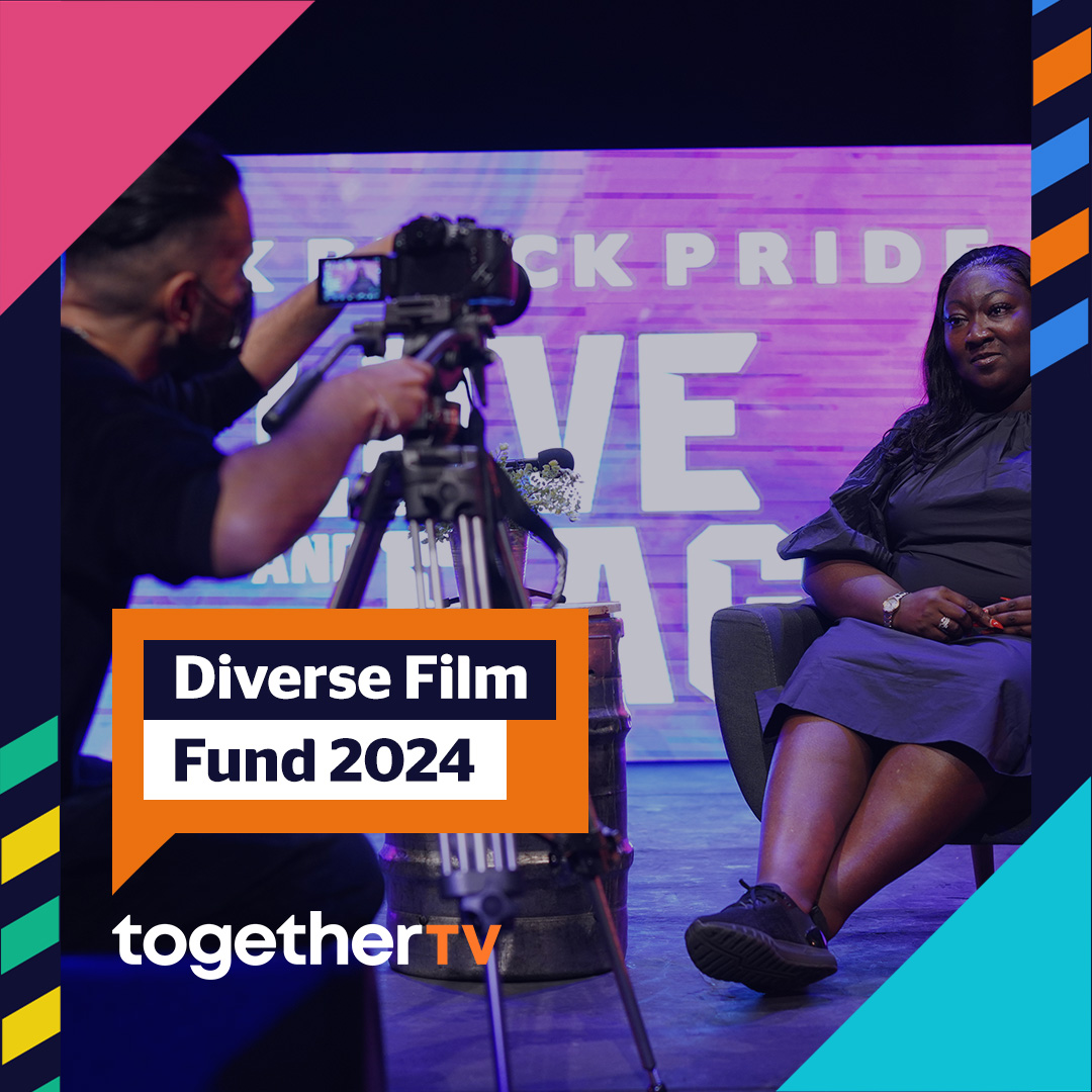 In the foreground of the photo there is a man with short, dark brown hair, in a black t-shirt operating a film camera on a tripod that is painting towards a black woman with long black hair wearing a black dress, black sneakers, a watch, and long orange nails. Text that appears on the photo reads: Diverse Film Fund 2024 in an orange speech bubble with a logo reading together TV underneath it.